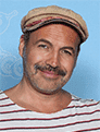 Billy Zane wearing a striped t-shirt and a cap smiling